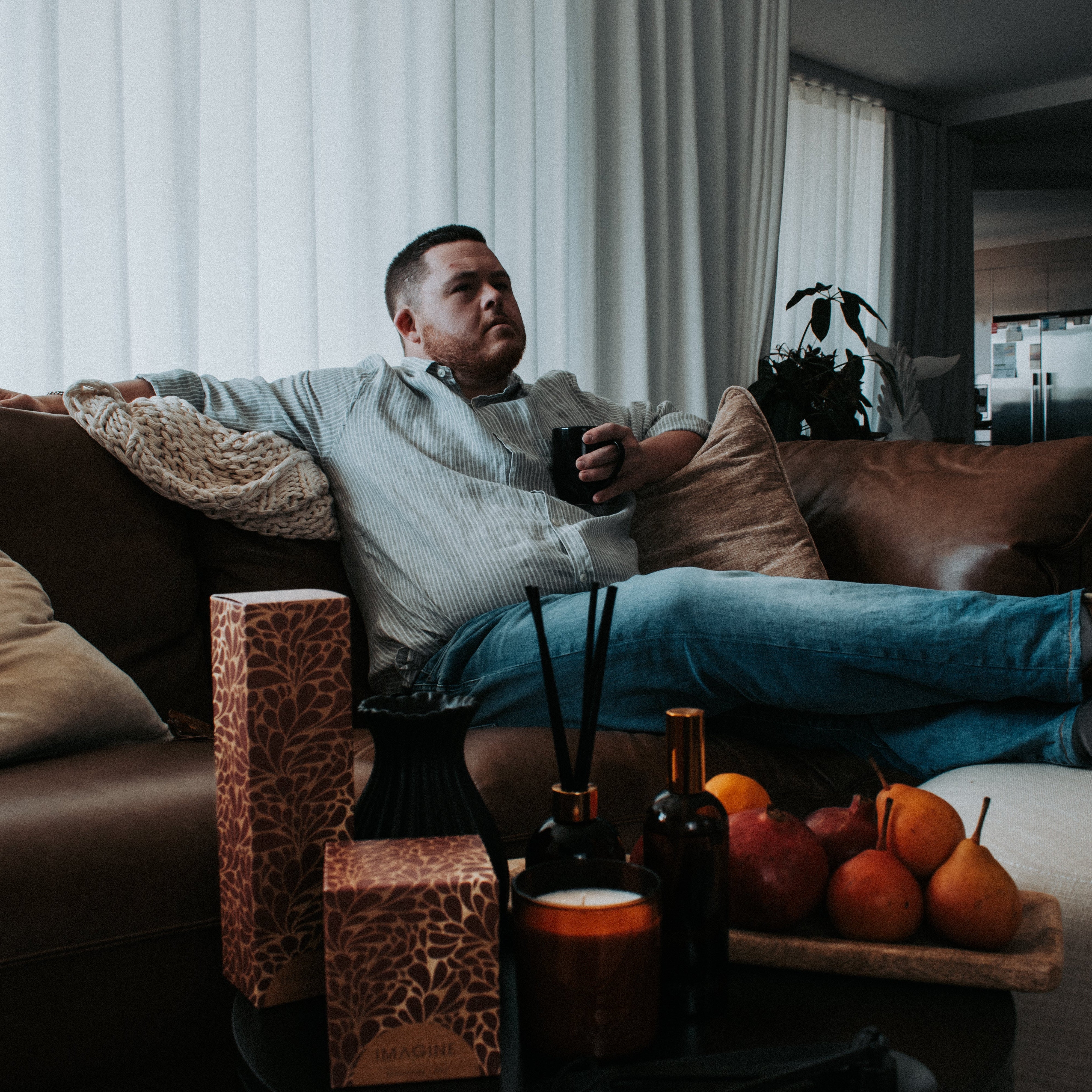 Man with down syndrome sitting on a couch in a living room with IMAGINE products positioned on a coffee table with fruit.